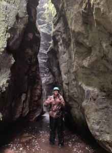 Anna standing at the bottom of a gulch, with tall cliffs on either side.