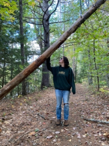 Maddie is standing in the forest and resting her hand on a tree that has fallen across the trail.